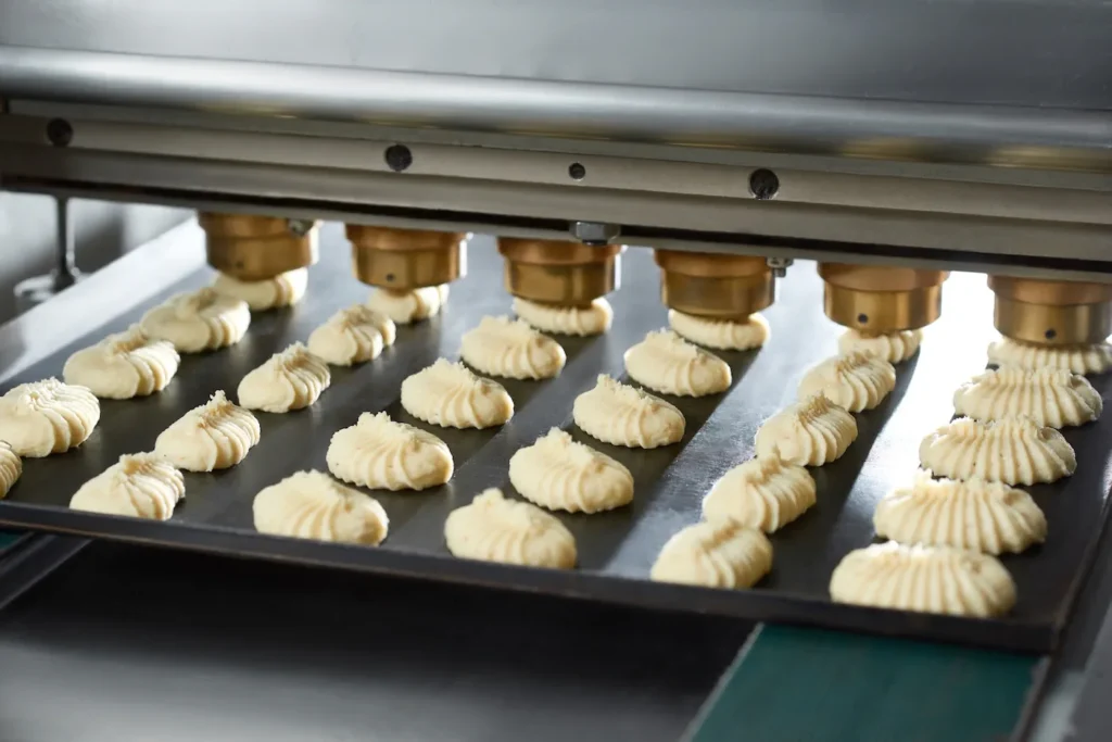 Close-up of conveyor line s equipment ,making little identical cakes from raw dough. They lie on the black dish on the conveyor line in the bakery. 